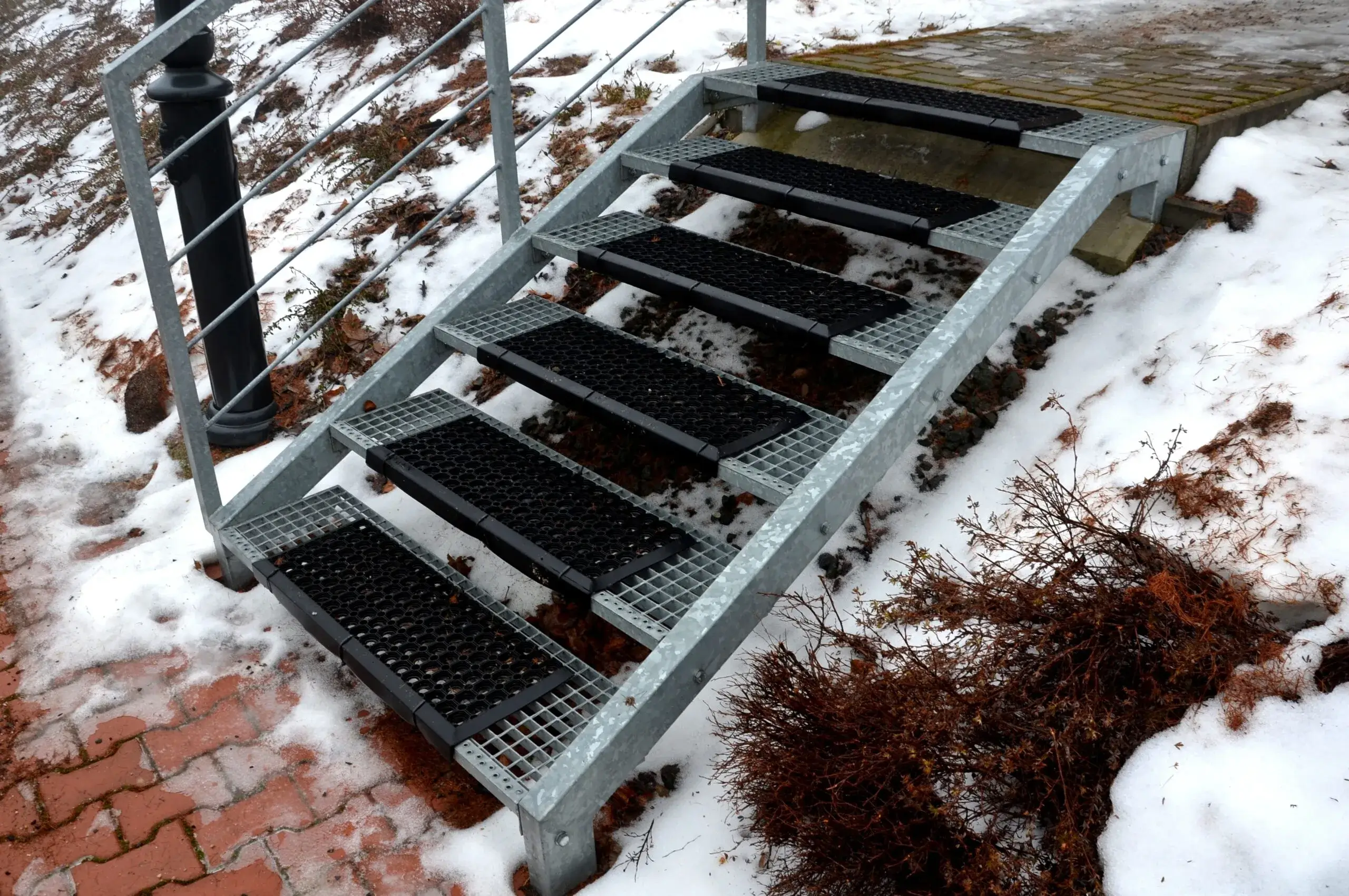 Buitentrap met zwarte rubber antislipmatten op metalen treden in winterse omstandigheden